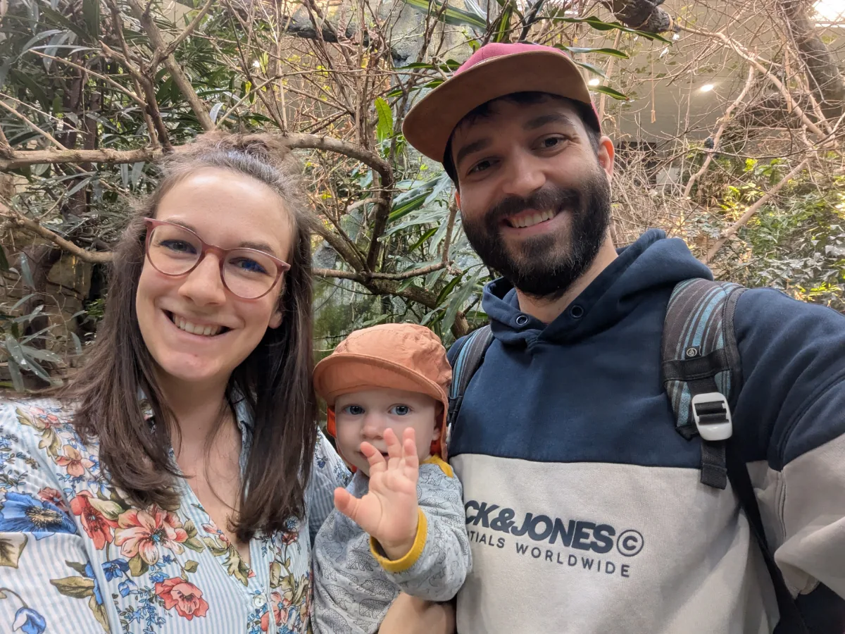 Christian with his wife and their young daughter, smiling, among tropical plants.